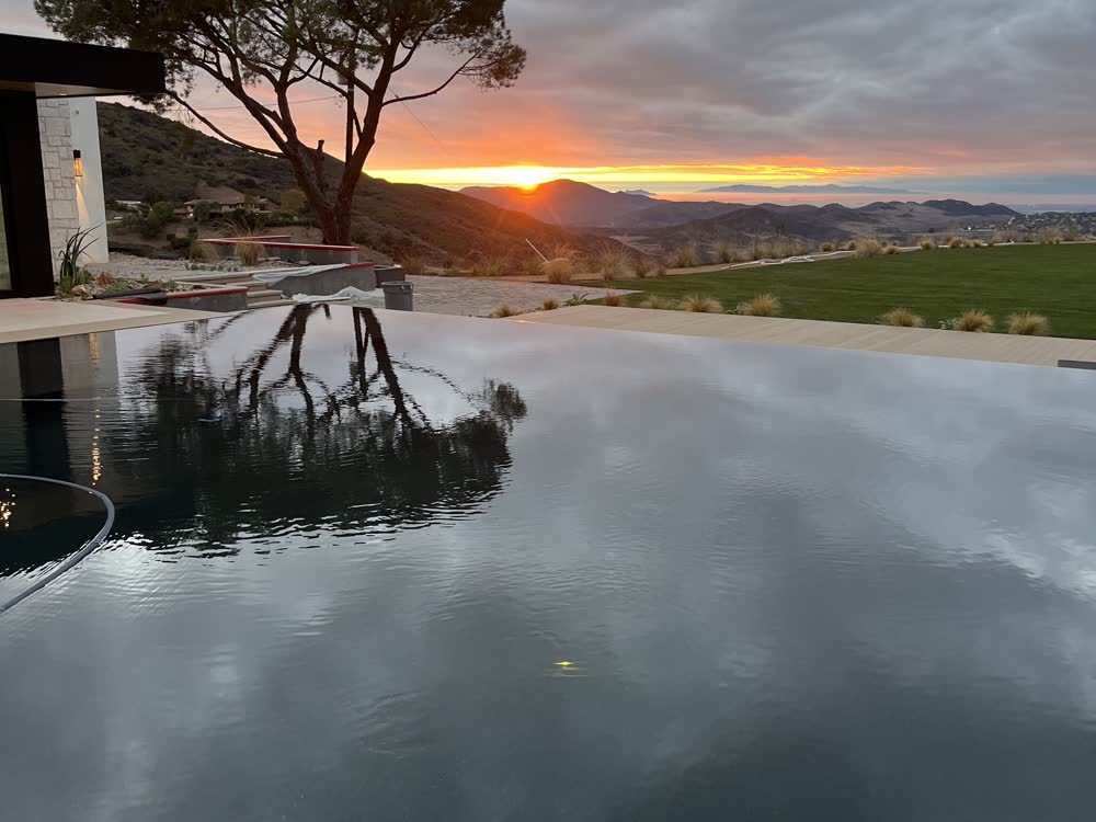 Sunset over the valley reflected in an infinity pool at dusk